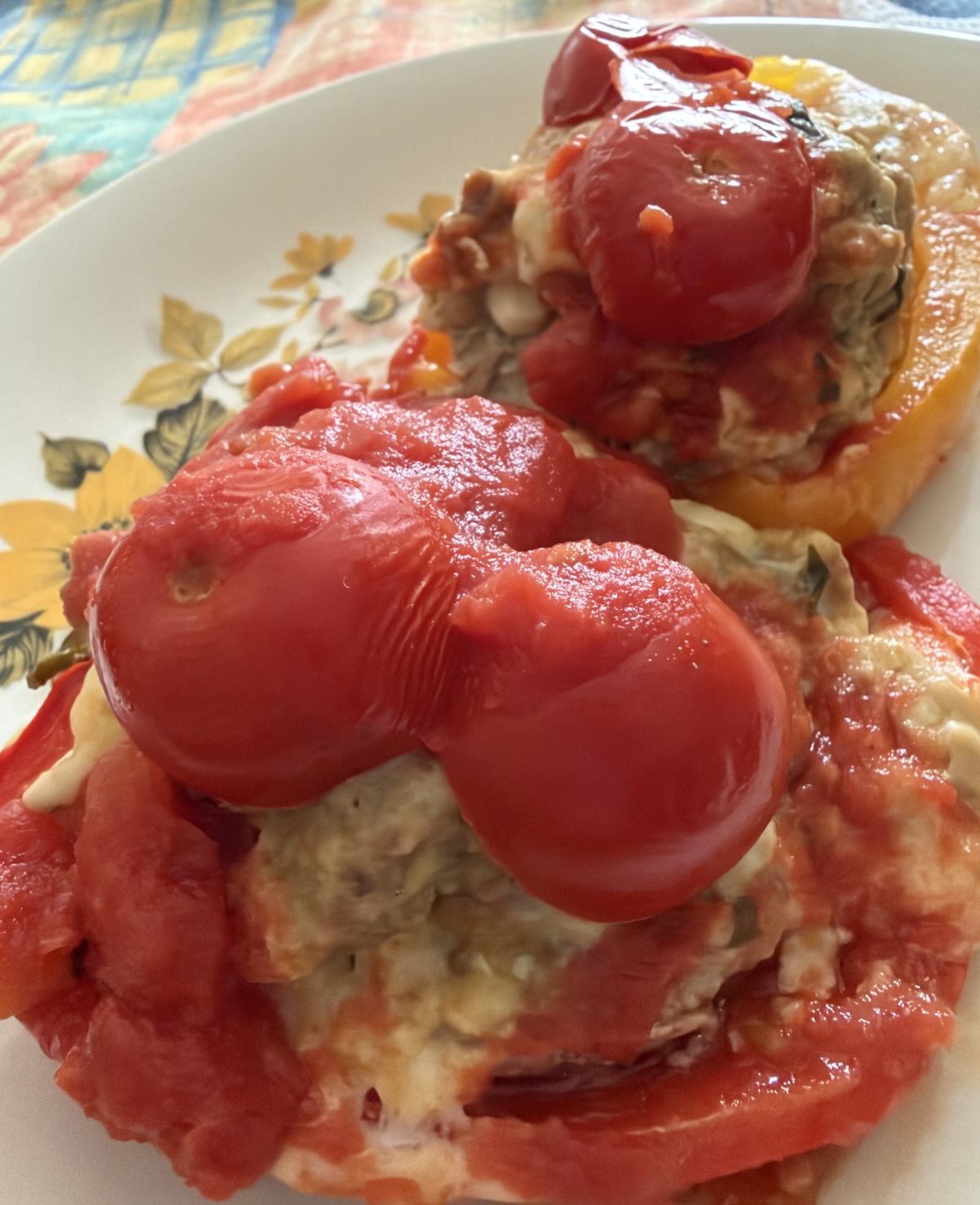 Peperoni rossi e gialli ripieni di carne, cotti al forno con formaggio fuso e pomodori pelati interi